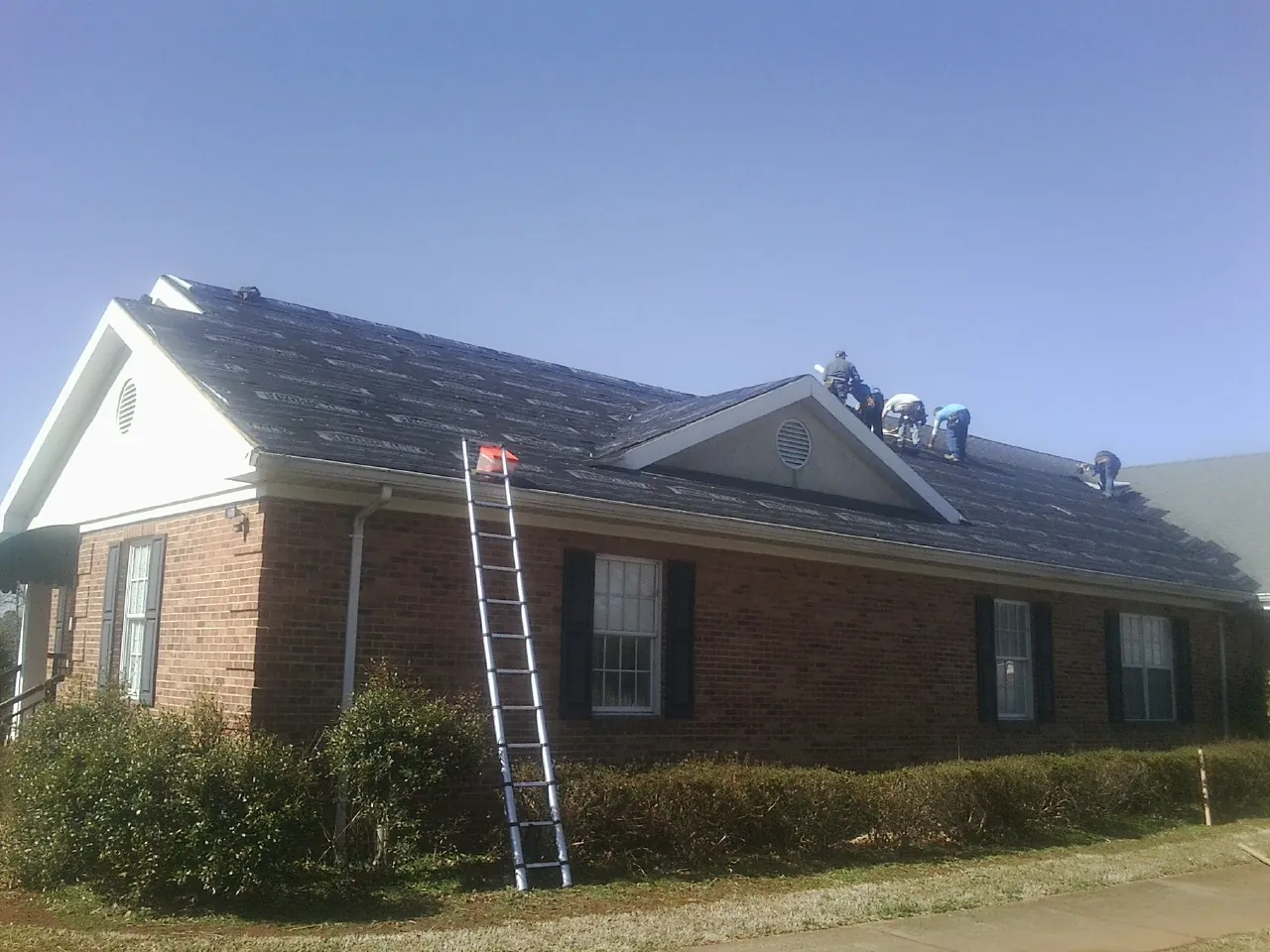 Crew tearing shingles off a brick ranch roof with a ladder set — Emergency Roof Repair work by our crew in Alto