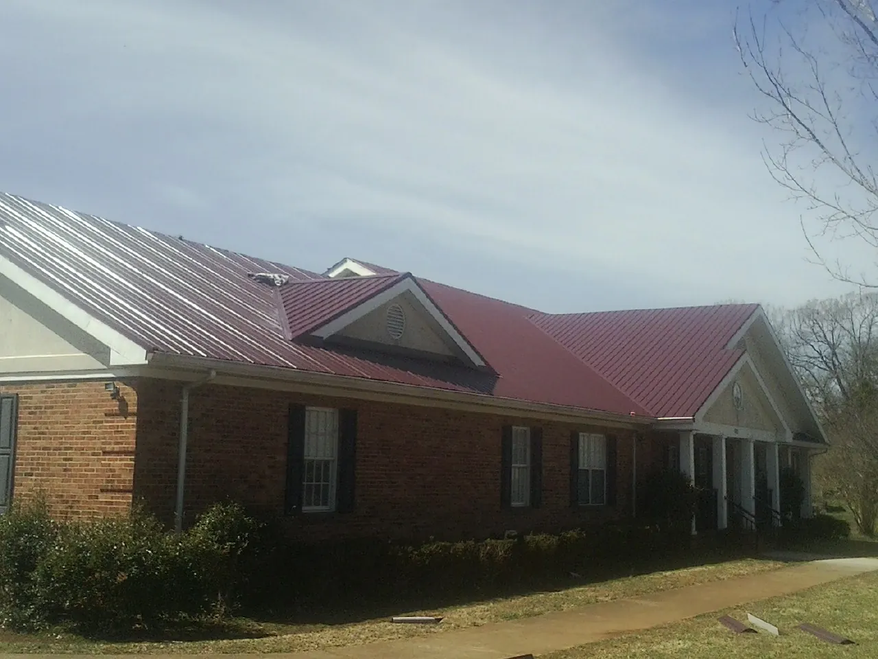 Red metal roof with gabled entries on a long brick building, from a Hail Damage Roof Repair job in Alto